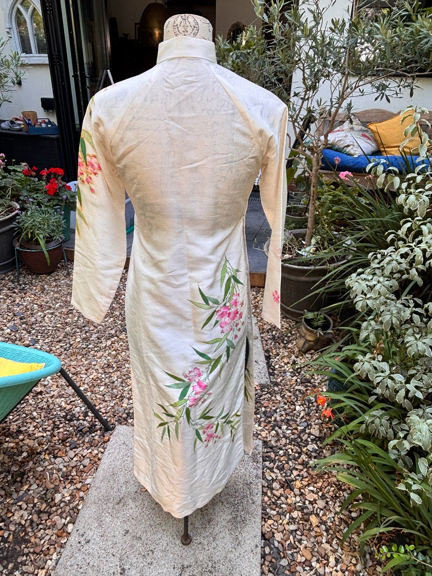 Otoch traditional off-white silk Ao Dai with hand-painted pink floral and green bamboo motifs on a dress form.