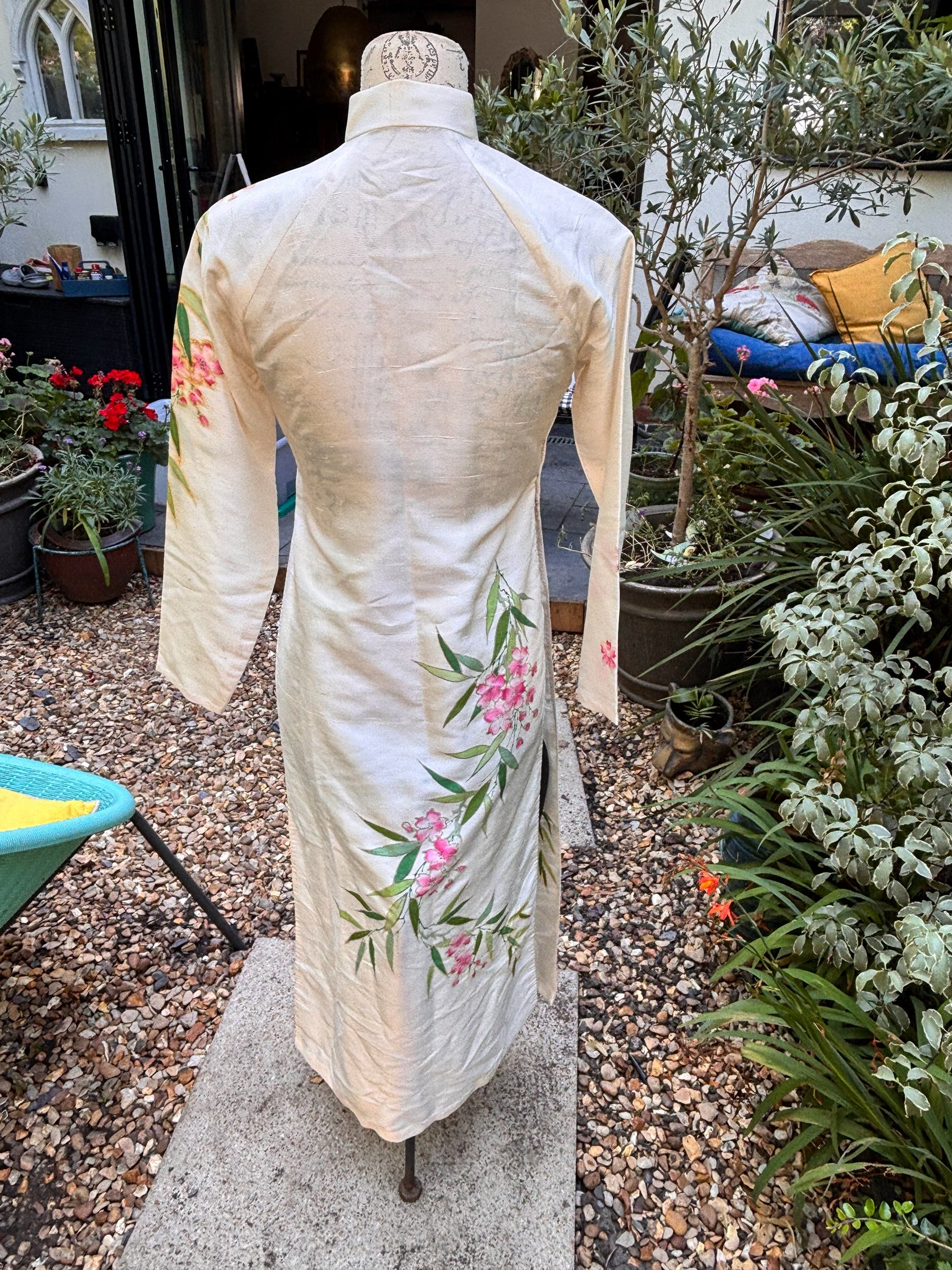 Otoch traditional off-white silk Ao Dai with hand-painted pink floral and green bamboo motifs on a dress form.