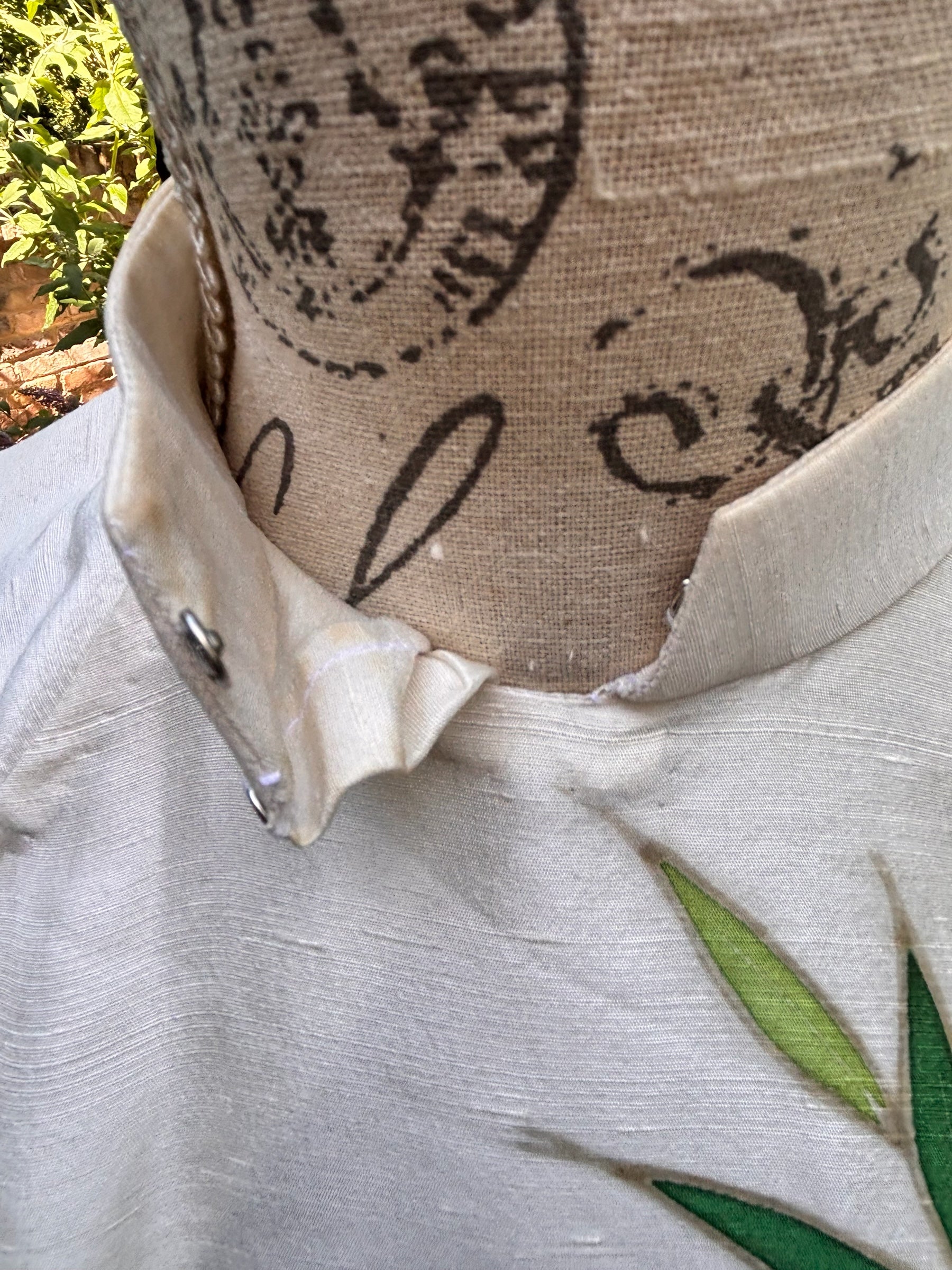 Otoch off-white silk Ao Dai featuring a mandarin collar and hand-painted green bamboo leaf detail on a mannequin.