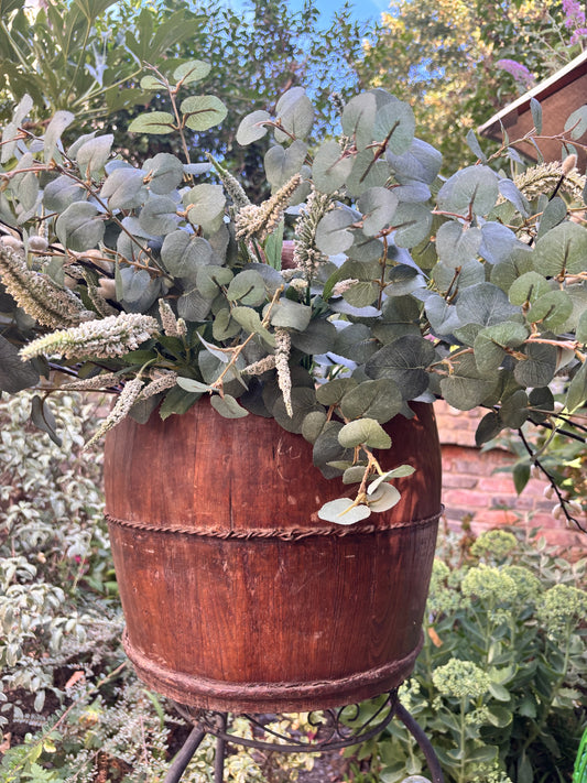 Otoch vintage dark wood decorative bucket filled with faux eucalyptus and white botanicals in a garden setting